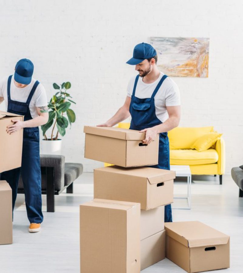 two-movers-in-uniform-carrying-cardboard-boxes-in-modern-apartment-1